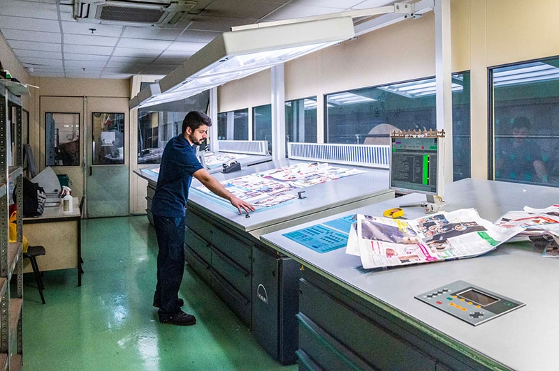 Des contrôles qualité sont effectués par des prélèvements tout au long de la ligne de fabrication. Ici, un conducteur effectue des retouches couleur sur le pupitre à encres.