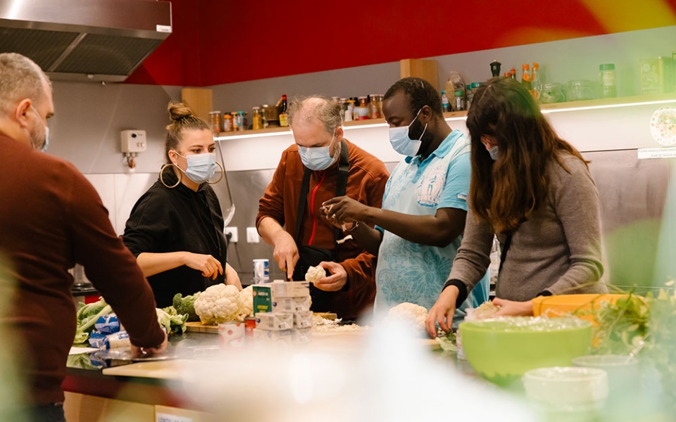 Chloée, salariée du Clubhouse de Paris explique aux membres Emmanuel et Brahima la recette du jour, pour la préparation de repas.