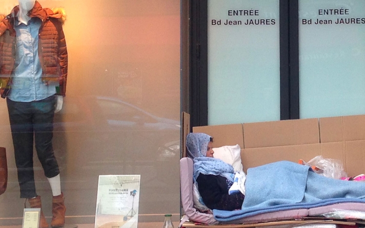 Femme dormant à la rue devant une vitrine de magasin.